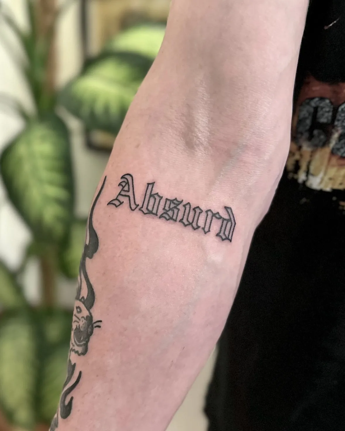 Tatuaż lettering Absurd z grubym konturem na przedramieniu — tatuaż, Wujek Darek, Warszawa, Polska